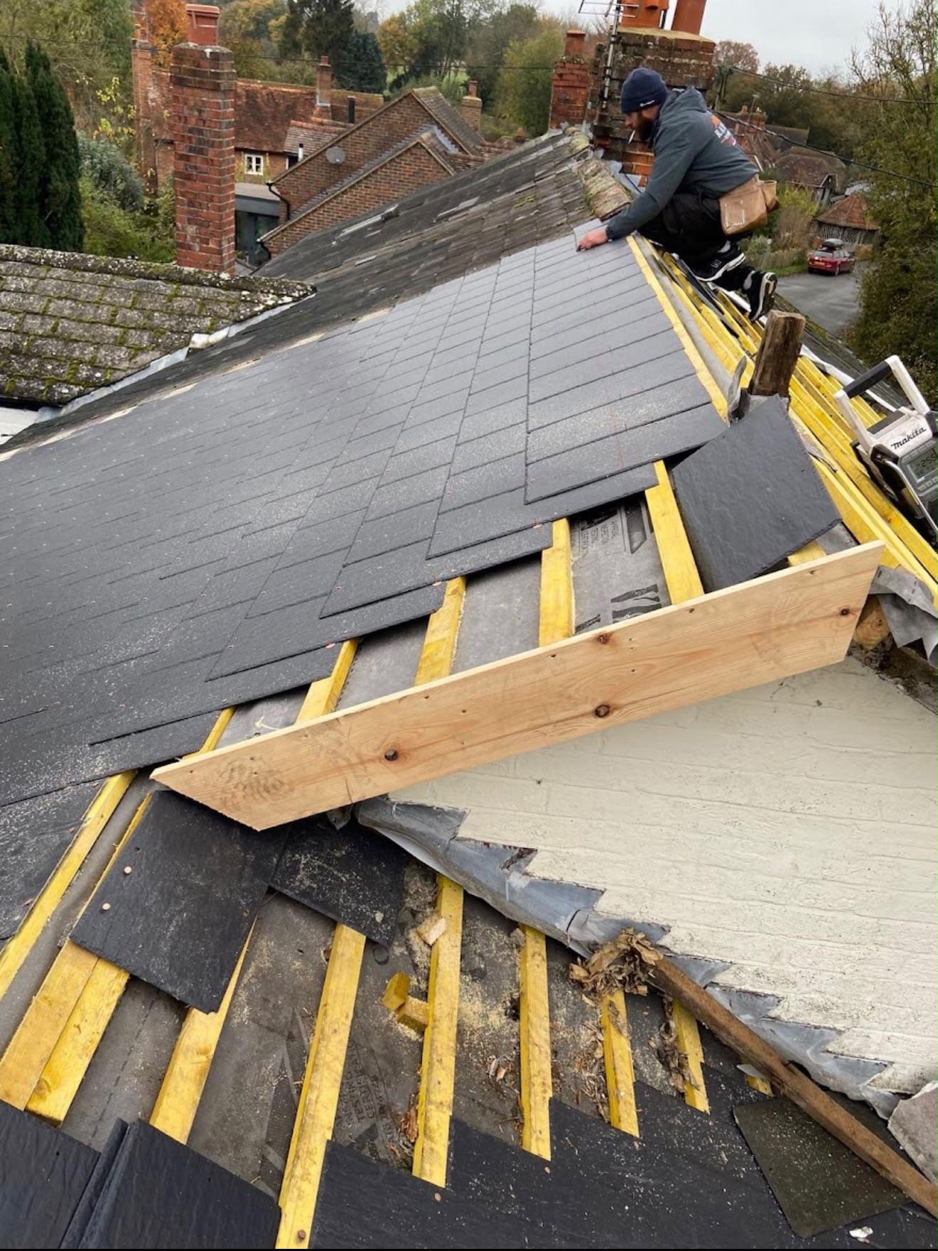 Roofer laying dark grey slate tiles over yellow marker battens