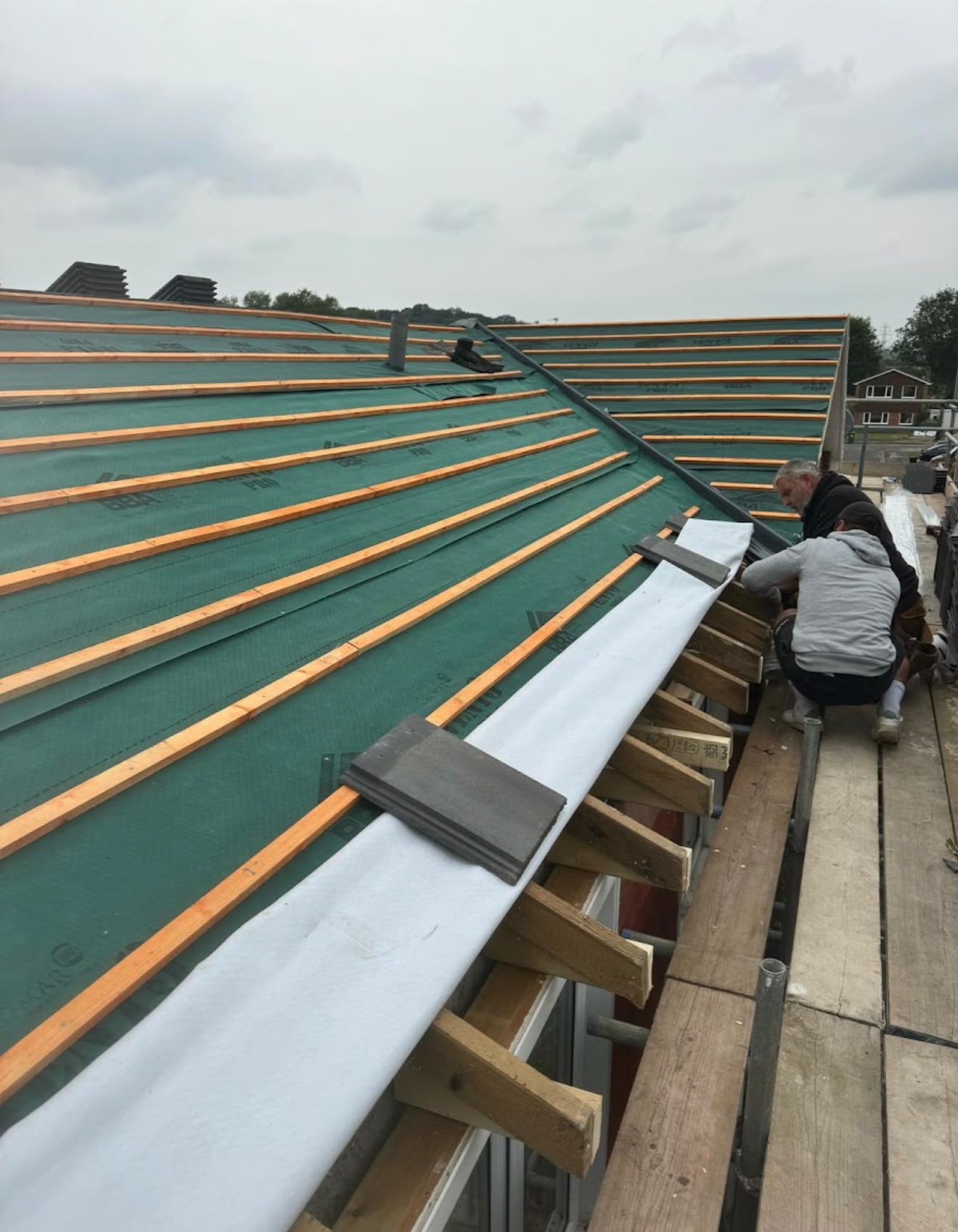 Roofers laying clay ridge tiles over new membrane and battens